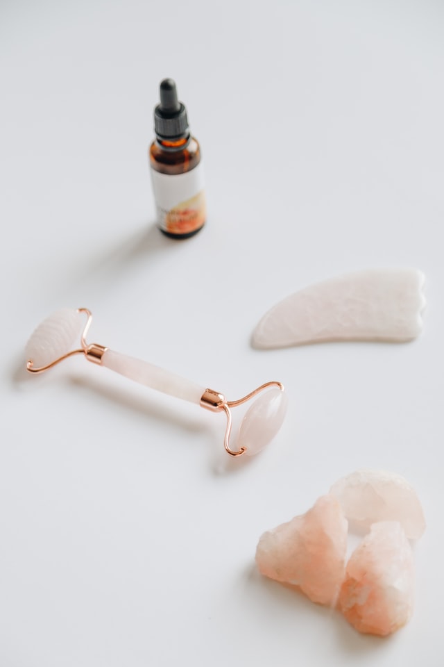 pink jade roller next to rose quartz crystals and small bottle