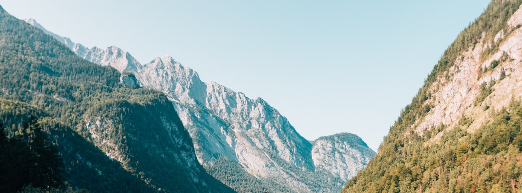 photograph of nature landscape with mountains, trees and sun behind clouds