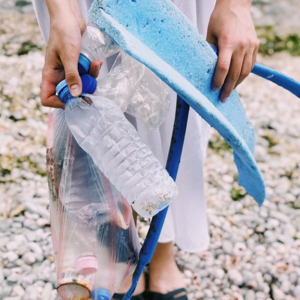 woman picking up trash and holding plastic bottles and hose