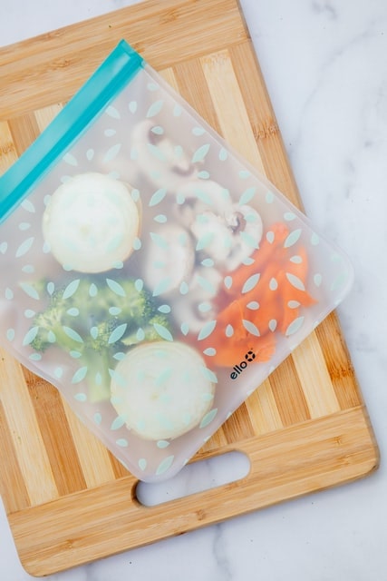 silicon food bag on top of wooden cutting board filled with carrots, mushrooms, broccoli, and onions
