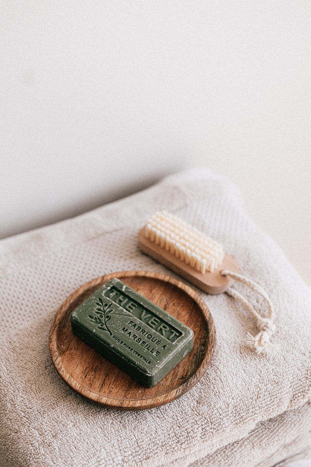 green soap bar on wooden plate next to exfoiliating brush