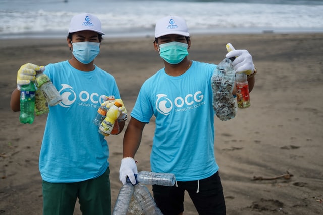 two men picking up trash and plastic on the beach